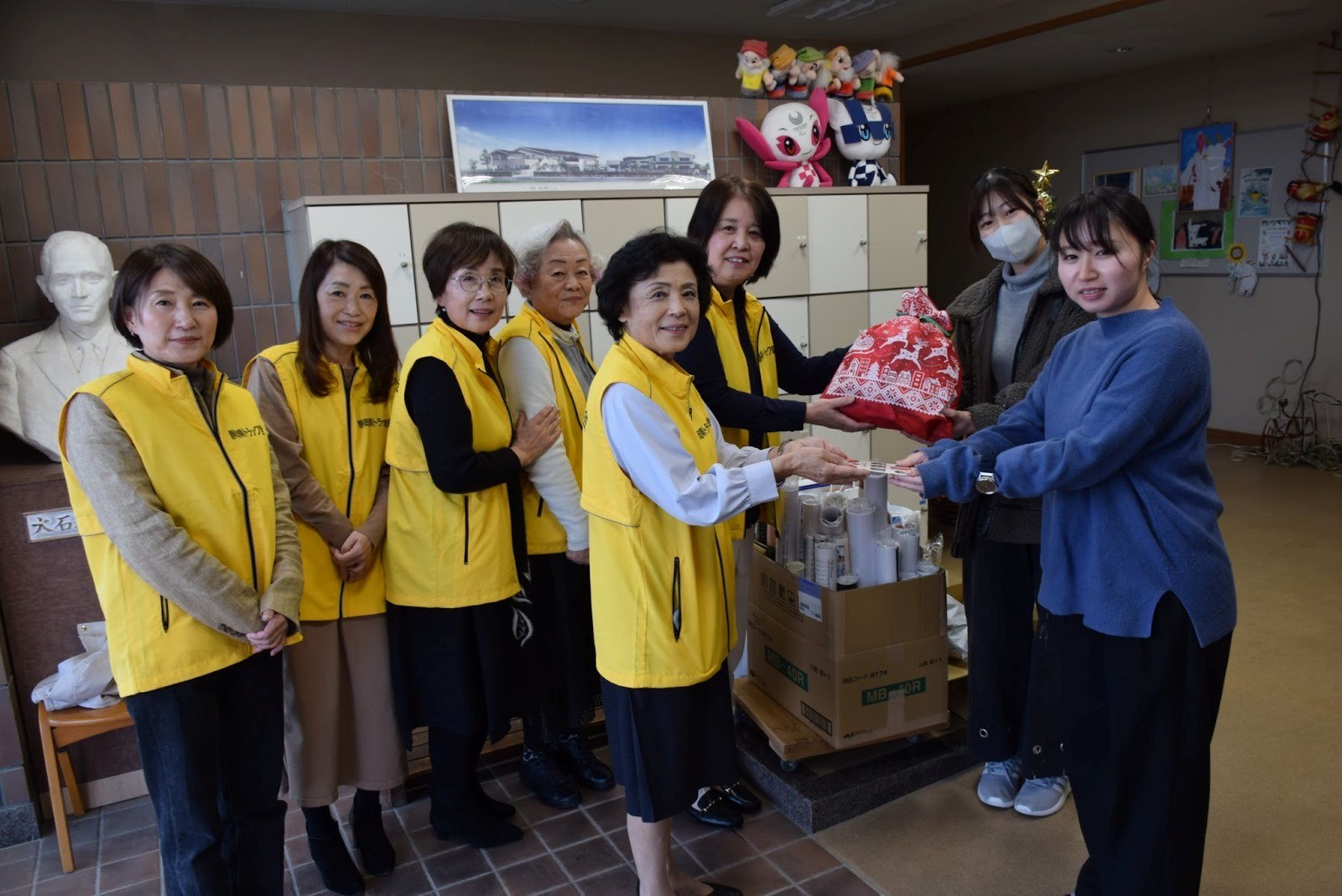 児童養護施設の職員にプレゼントを手渡す鈴木部会長（後列右から2人目）ら