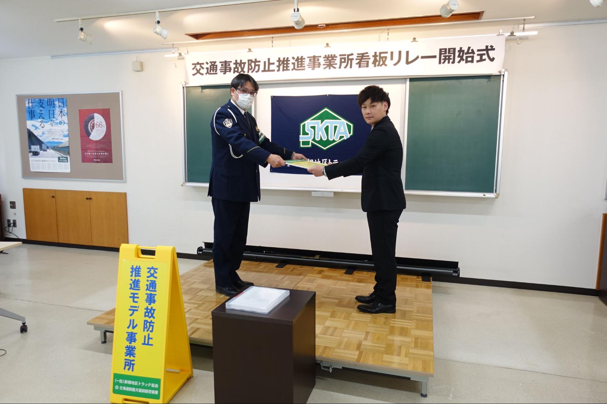 釧路署の大城戸交通官㊧から看板とパネルを受け取る内陸運送の和田課長