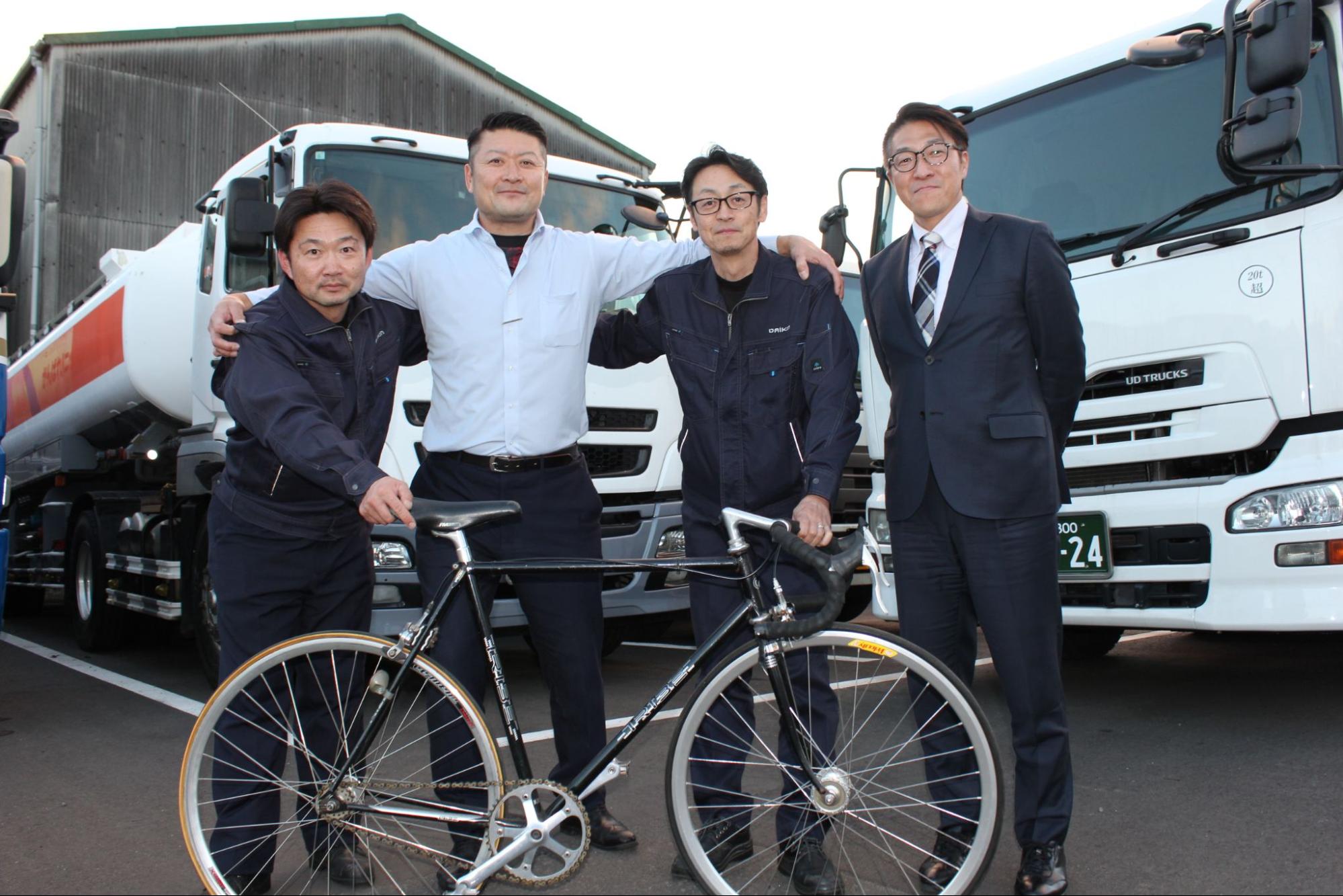 大型タンクローリーの前で肩を組む（左から）和田乗務員、大熊社長、盛田乗務員と関戸市議