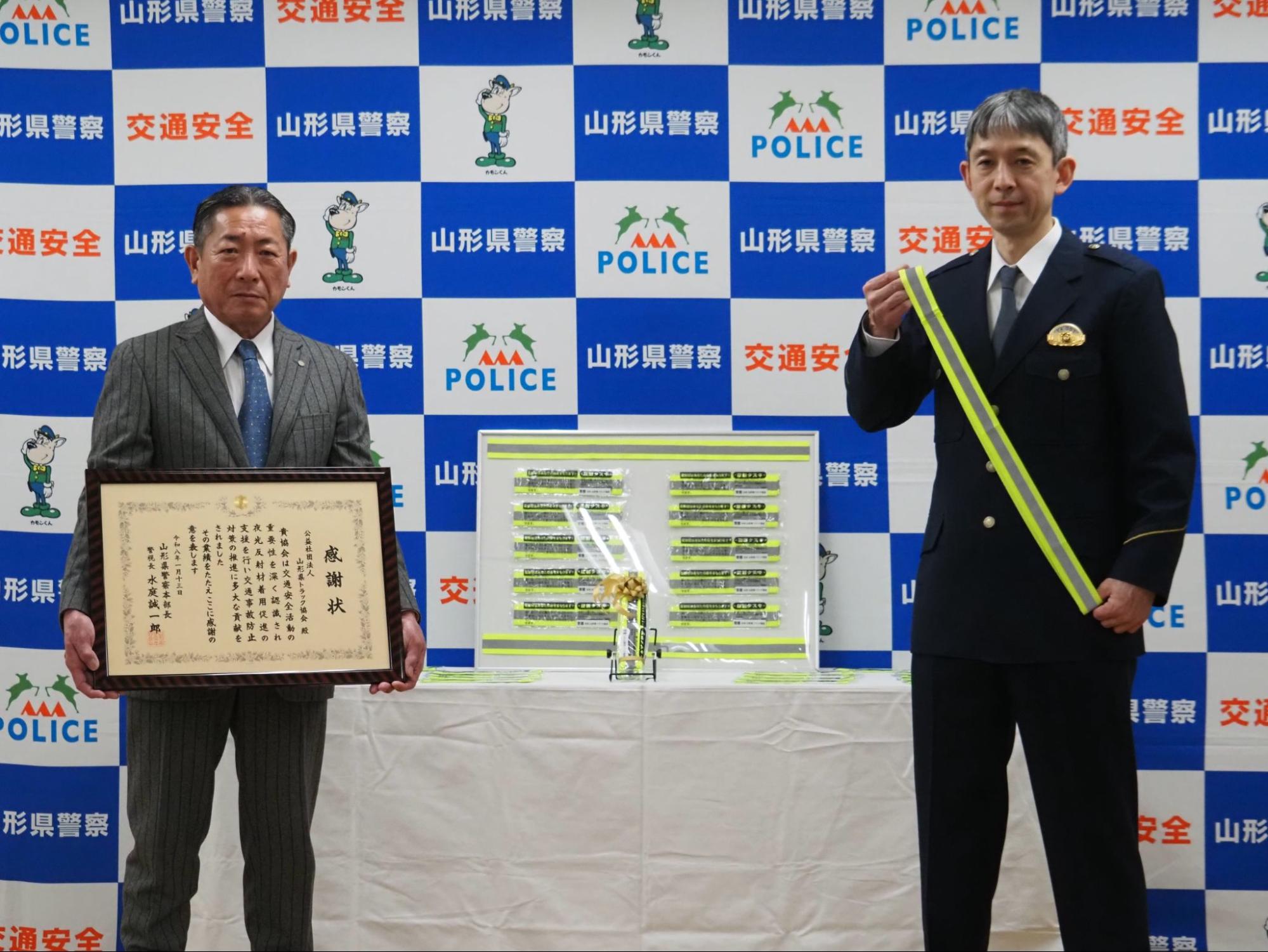 感謝状を手に熊澤会長、たすきを持つ県警の水庭本部長