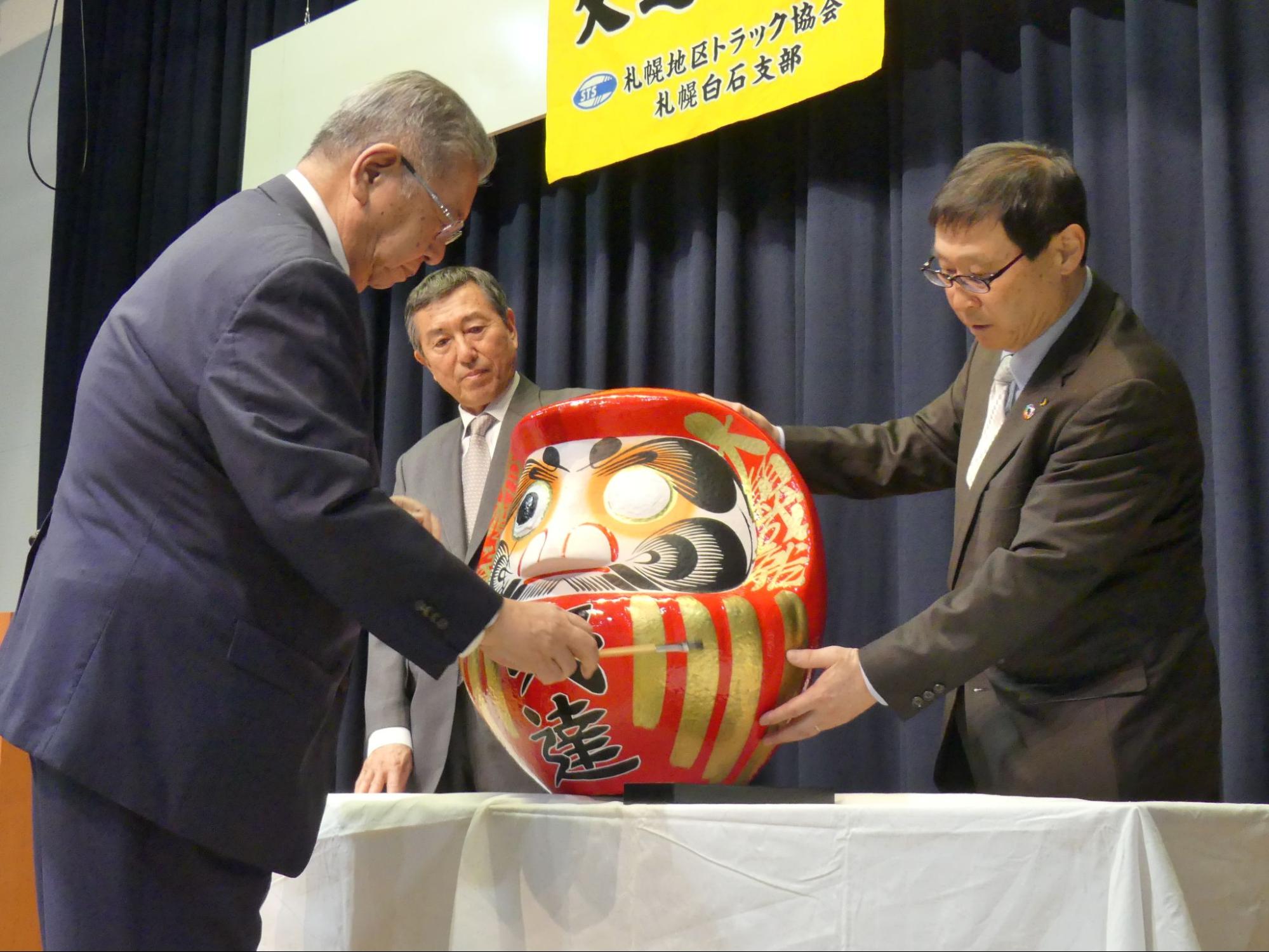 だるまに墨で目を入れる（左から）中村支部長と、坪田、佐々木の両副支部長