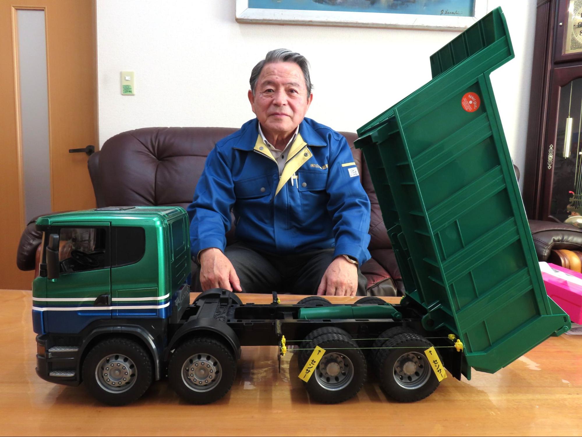 山城運輸仕様のトラックと車両用脱輪防止装置の模型を前に加藤社長