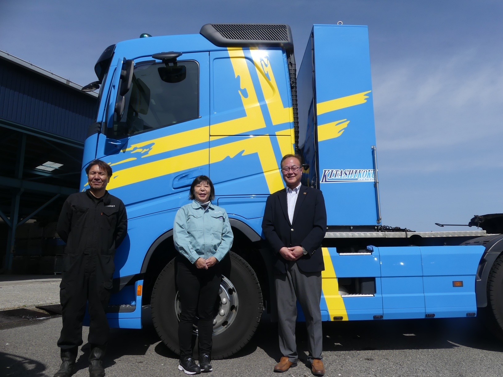 新デザイン車両をバックに岡社長（中央）、九鬼室長（右隣）、ドライバー