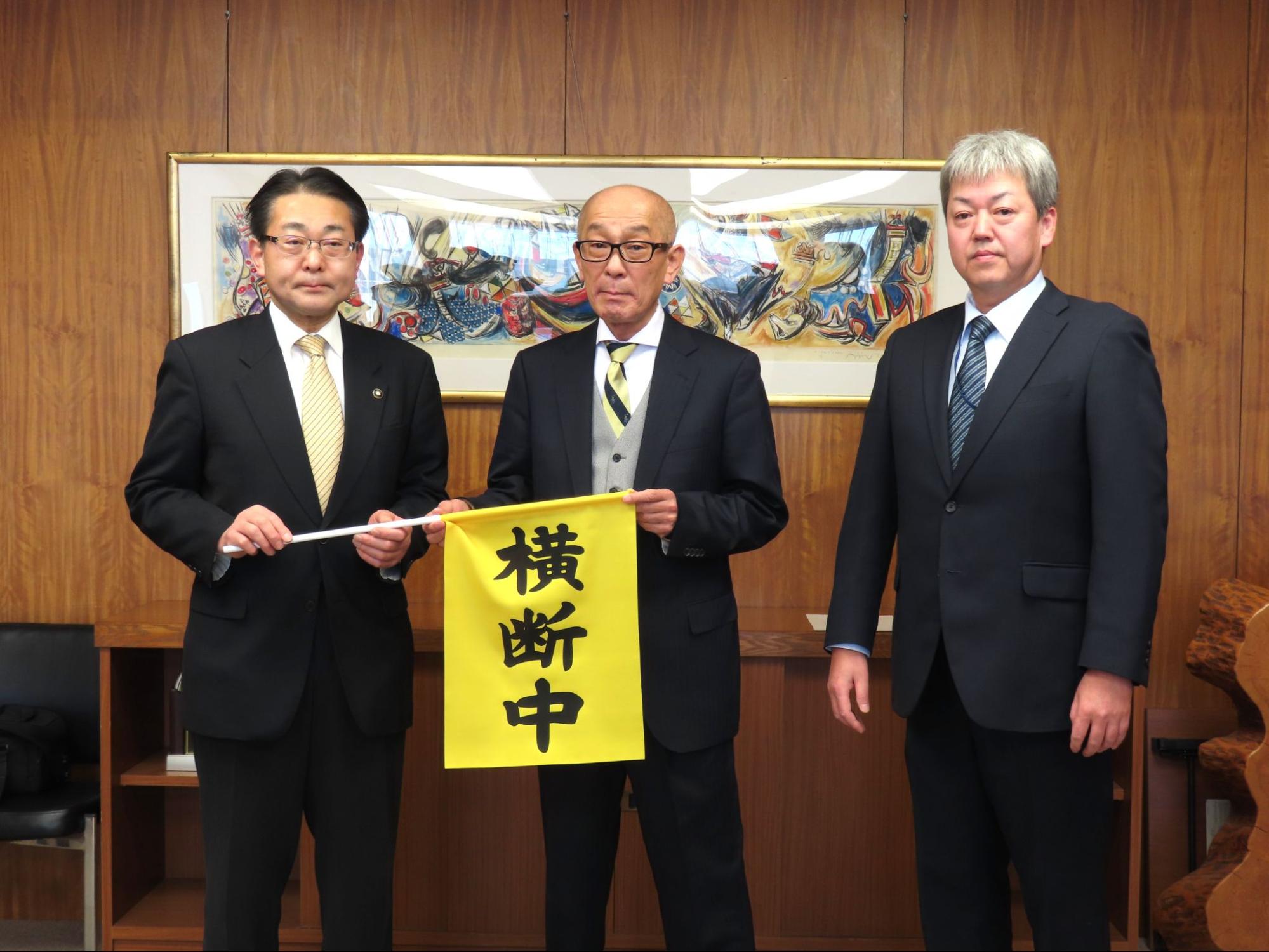 横断旗を持つ八重樫市長（左端）と高橋支部長、鎗水副支部長（右端）