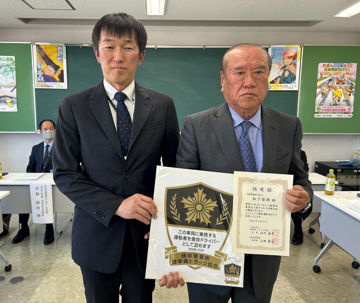 認定証とステッカーを持つ清水委員長㊨と県警の今村課長補佐