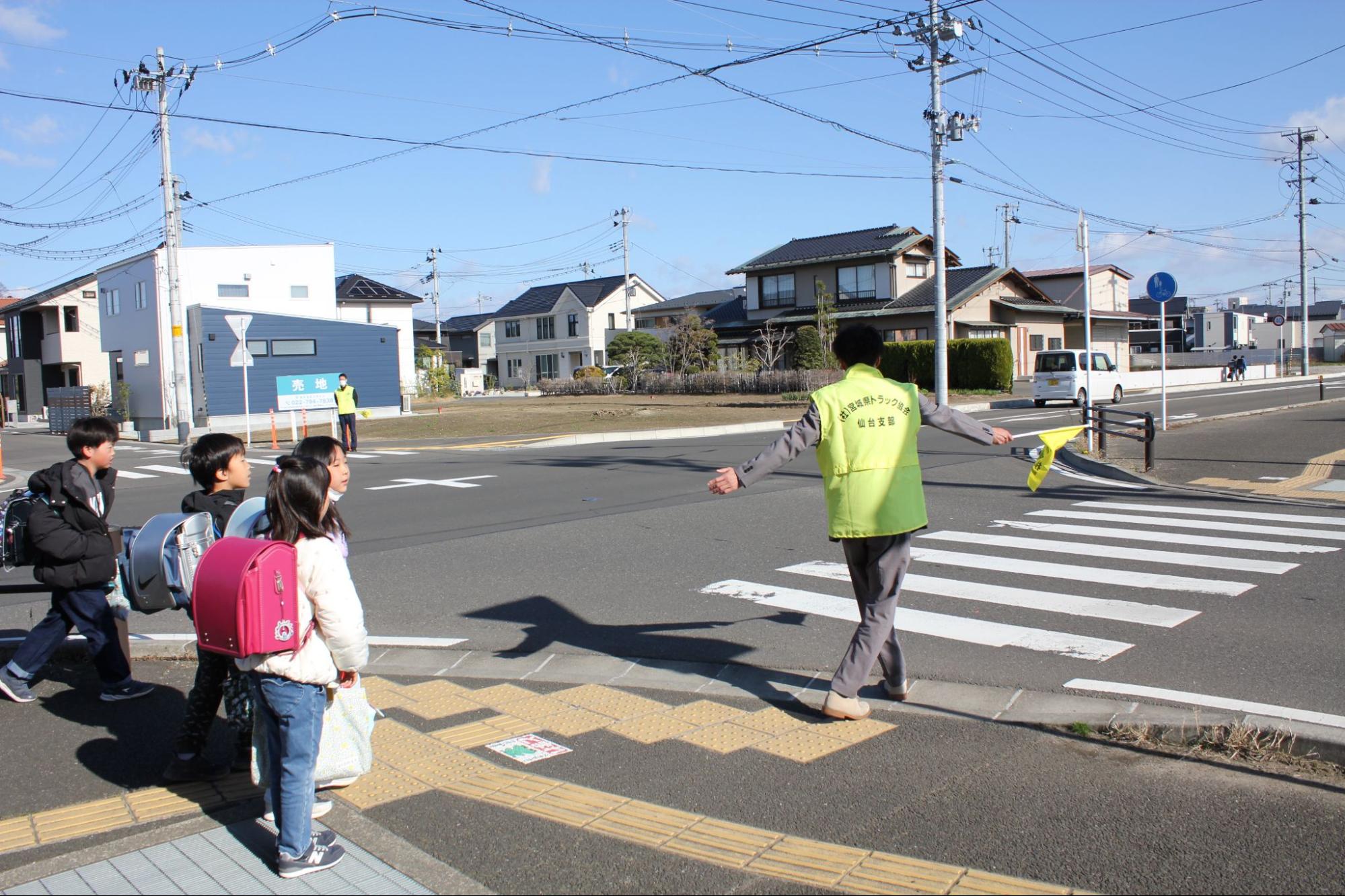 登校する児童を安全に横断させる宮ト協仙台支部青年部員ら（8日）