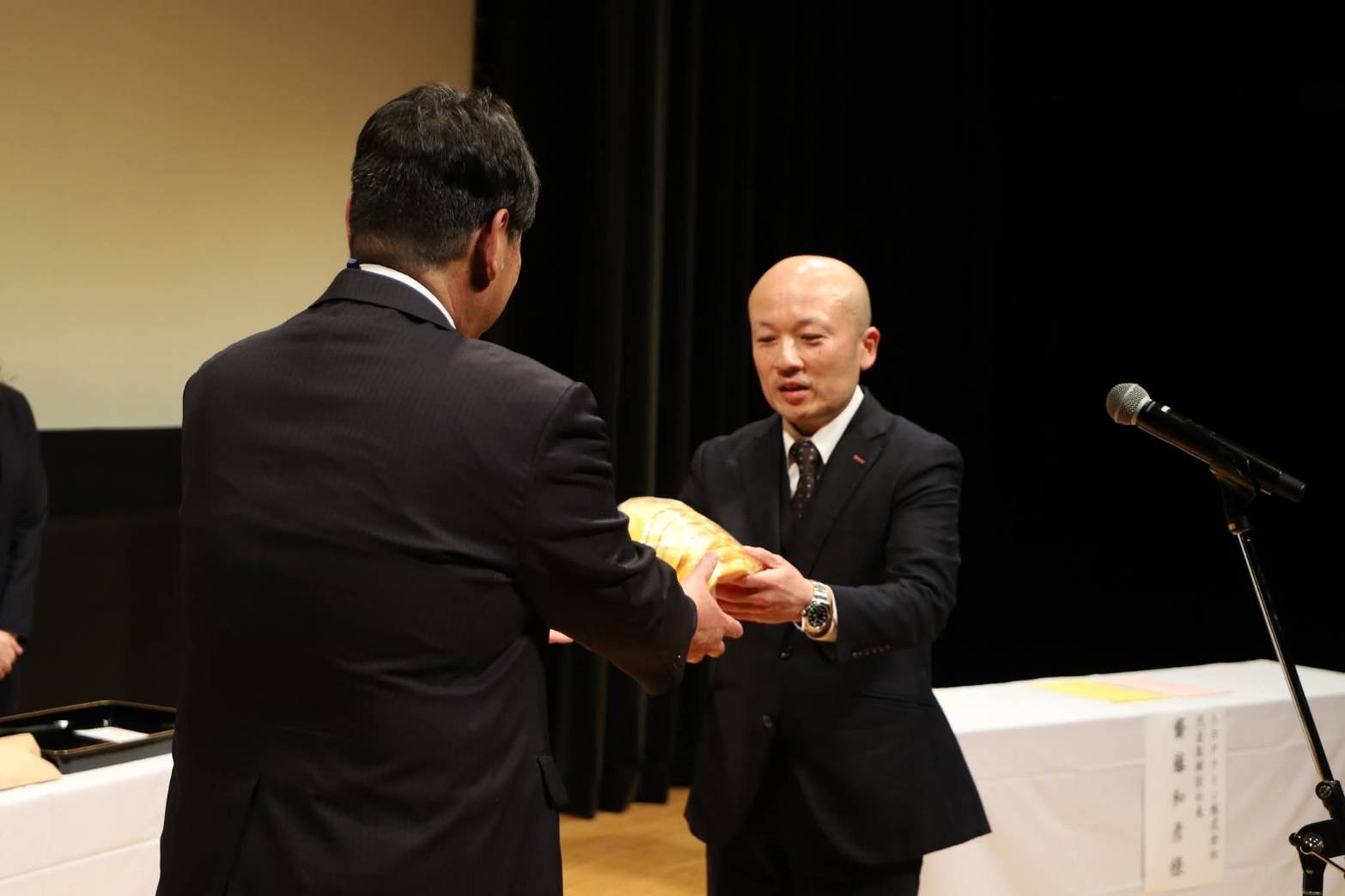 大石田町教委の鈴木委員長（手前）に帽子を手渡す齋藤社長
