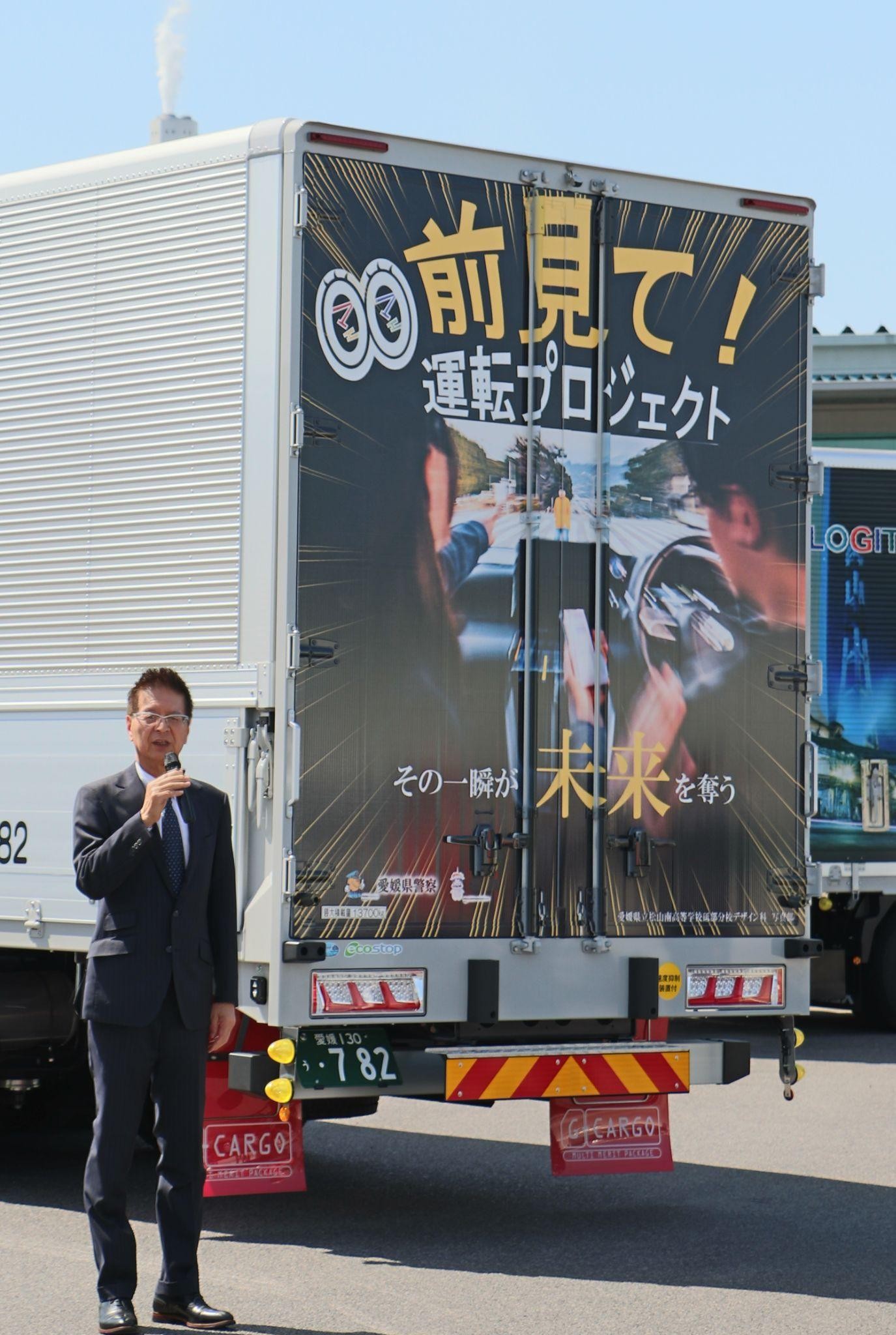 デザイントラックをバックにあいさつする西岡社長