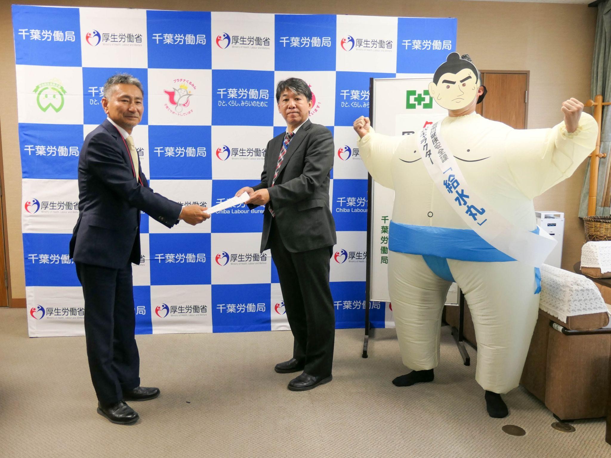 大里支部長㊧に要請文を手渡す小山局長、千労局オリジナルキャラクターの給水丸