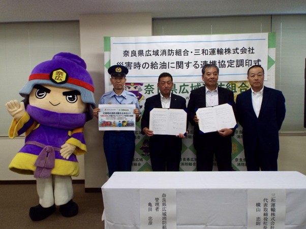 調印書類を手にする奈良県広域消防組合の亀田管理者（右から3人目）と三和運輸の横山社長（右隣）