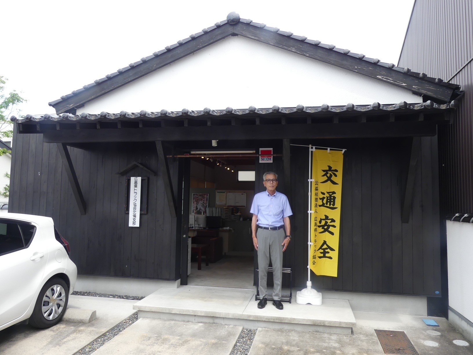 黒塗りの板を張った正面玄関の前に立つ菟原事務長