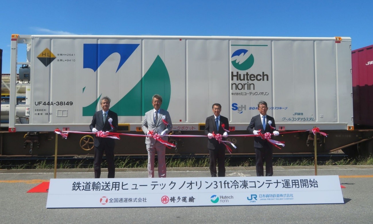 コンテナを背にテープカットする4社の社長