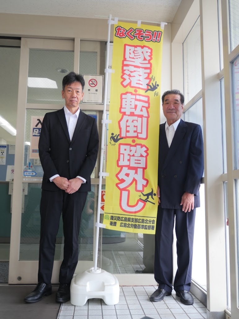 のぼり旗と並ぶ岡野分会長㊨、岡野署長